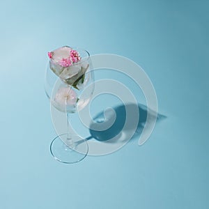 Beautiful small pink flowers in transparent glass on blue background with copy space