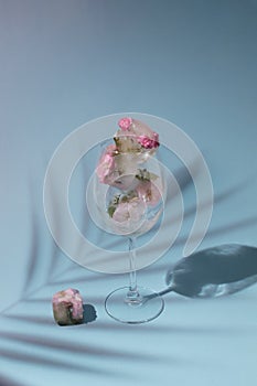 Beautiful small pink flowers in transparent glass on blue background with copy space. Sunny day concept