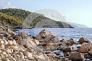 Beautiful small rocky beach with clear blue sea, waves and mountains on background. Oludeniz, Turkey