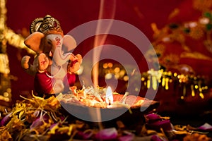 Beautiful small statue of lord ganesha with clay lamp on rose petals against red golden background. hinduism and religion concept