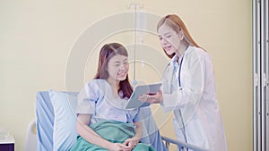 Beautiful smart Asian doctor and patient discussing and explaining something with tablet in doctor hands while staying on Patient