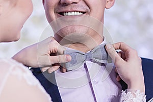 A beautiful smile of a guy in a blue suit, when the girl`s hands adjust the gray bow tie.