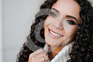 Beautiful smile white-toothed and gorgeous smoky shading green eyes of curly brunette. close-up