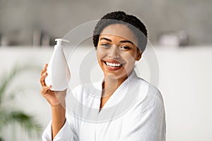 Beautiful Smiling Black Woman In Bathrobe Holding Bottle With Moisturising Body Lotion, photo