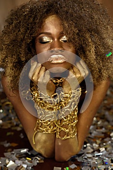 Beautiful smiling african american woman in gold accessories with arms crossed under her chin on bright background