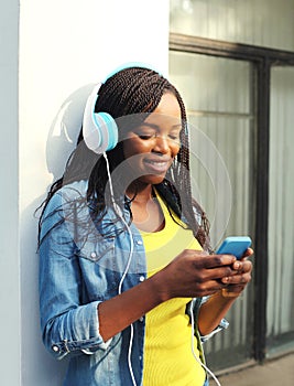 Beautiful smiling african woman with headphones listens to music and using smartphone