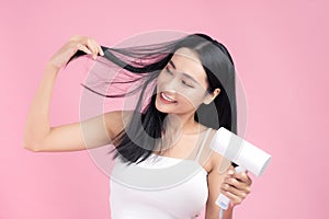 Beautiful Smiling Asian Girl With Black Long Straight Hair Using Hairdryer. Isolated on pink background