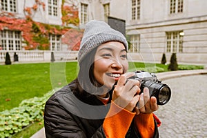 Beautiful smiling asian woman taking pictures with vintage camera while sitting in old city