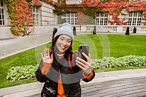 Beautiful smiling asian woman taking selfie on mobile phone and waving while sitting in old city