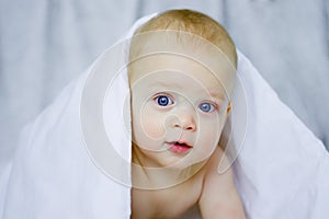 Beautiful smiling baby child after bath. Cute toddler on the bed under the blanket