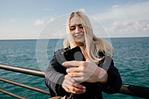 A beautiful smiling blonde girl makes a selfie on the phone against the background of the sea.