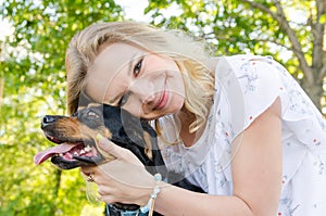 A beautiful smiling blonde young woman in a light dress with tenderness hugs her cute dog