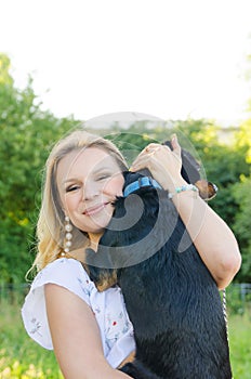 A beautiful smiling blonde young woman in a light dress with tenderness hugs her cute dog. Vertical view