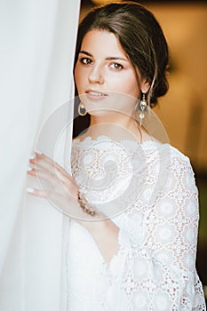 Beautiful smiling bride brunette young woman in white lace dress near window, close up portrai