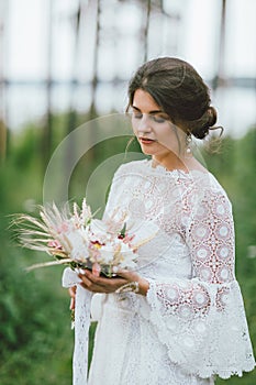 Beautiful smiling bride brunette young woman in the white lace dress with wedding boho bouquet, close up portrait outdoors