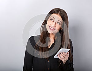 Beautiful smiling brunette woman in black style shirt holding in hand, use mobile cell phone and thinking looking up isolated on