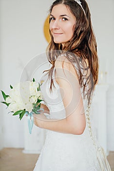 Beautiful smiling brunette woman bride in wedding dress with classical white roses bouquet in living room