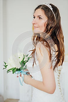 Beautiful smiling brunette woman bride in wedding dress with classical white roses bouquet in living room