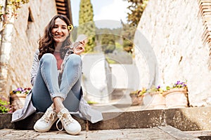 Beautiful smiling brunette woman sitting on the ground with a cup of coffee to go