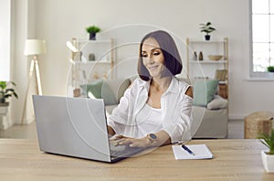 Beautiful smiling business lady working remotely in her home office using laptop.