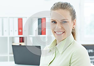 Beautiful smiling business woman sitting at office workplace half turn looking in camera portrait.