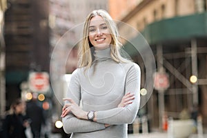 Beautiful smiling businesswoman with arms crossed standing outdoors on city street.