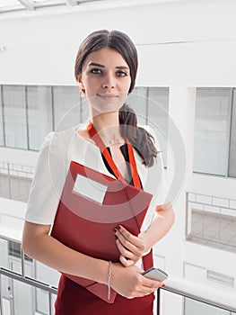 Beautiful Smiling Businesswoman Standing Against White Offices Background. Portrait of Business Woman With a Folder in Her Hands