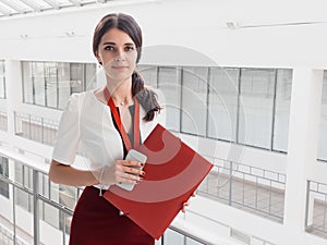 Beautiful Smiling Businesswoman Standing Against White Offices Background. Portrait of Business Woman With a Folder in Her Hands