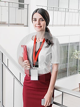 Beautiful Smiling Businesswoman Standing Against White Offices Background. Portrait of Business Woman With a Folder in Her Hands