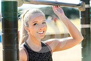 Beautiful smiling and cheerful portrait of a female athlete, exercising in city park with outdoor pull up bar course equipment