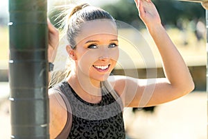 Beautiful smiling and cheerful portrait of a female athlete, exercising in city park with outdoor pull up bar course equipment
