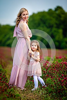 Beautiful smiling child girl with young mother in family look in field of clover flowers in sunset time