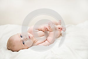 Beautiful smiling cute baby girl with blue eyes lying on the back on the bed in the room. Happy child laughing