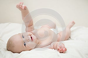 Beautiful smiling cute baby girl with blue eyes lying on the back on the bed in the room. Happy child laughing
