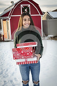 Beautiful smiling Diverse teen girl delivery a Christmas present to a friend. Holding a stack of wrapped presents and walking th