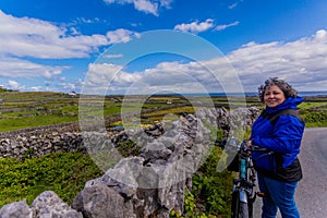 Beautiful and smiling female cyclist pausing on a road next to a stone fence on the Inis Oirr island