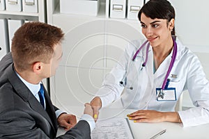 Beautiful smiling female medicine doctor shaking hands with male