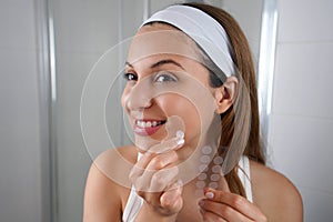 Beautiful smiling girl applying acne treatment patch on a pimple in bathroom