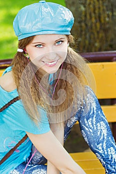 Beautiful smiling girl in a blue hat with pink headphones sitting in the Park on a bench and listening to music