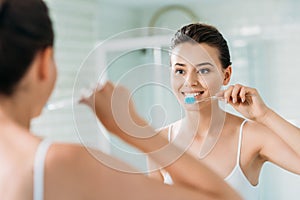 beautiful smiling girl brushing teeth at mirror photo