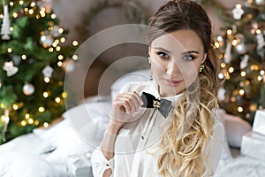 Beautiful smiling girl in evening attire near the New Year tree and with gifts. Festive hairstyle and makeup