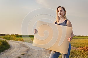 Beautiful smiling girl gets hitchhiked and votes with a sign of cars on a rural road in the rays of the sunset