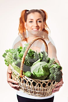 Beautiful smiling girl holding basket of fresh raw green vegetables isolated.