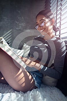 Beautiful smiling girl reading book and relaxing on her bed at home