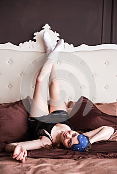 Beautiful smiling girl relaxing in bed at the morning. She is lying and having fun with legs up. Looking at camera