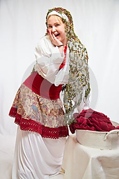 Beautiful smiling girl in stylized slavic red and white national costume washes the fabric in the basin on white