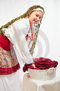 Beautiful smiling girl in stylized slavic red and white national costume washes the fabric in the basin on white