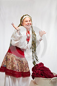 Beautiful smiling girl in stylized slavic red and white national costume washes the fabric in the basin on white