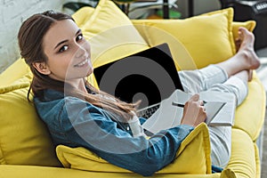 beautiful smiling girl using laptop and taking notes