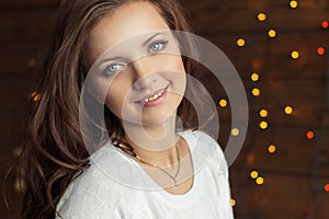 Beautiful smiling girl in warm white jacket sits near the window next to the wall in the lights